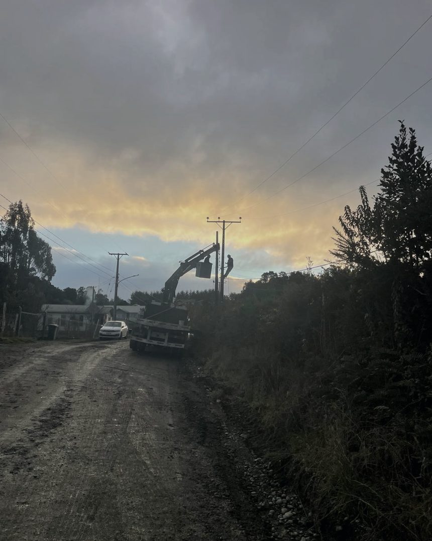 Camión grúa en faena eléctrica sobre un camino rural de Chiloé al atardecer